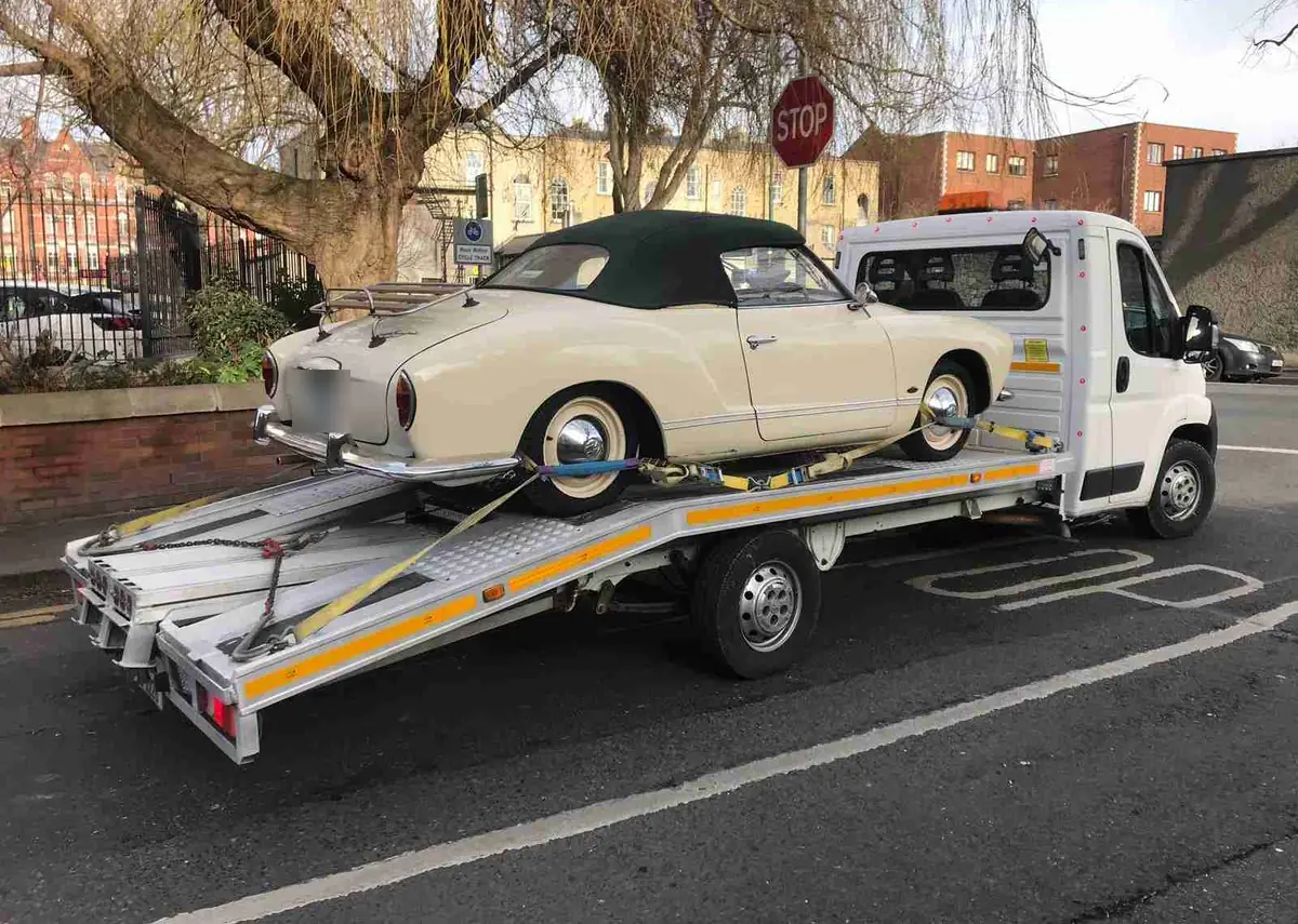 A cream classic convertible strapped onto a CC Recovery flatbed in a town car park
