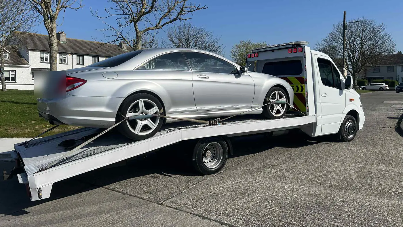 A silver coupe on the ramp of a recovery truck