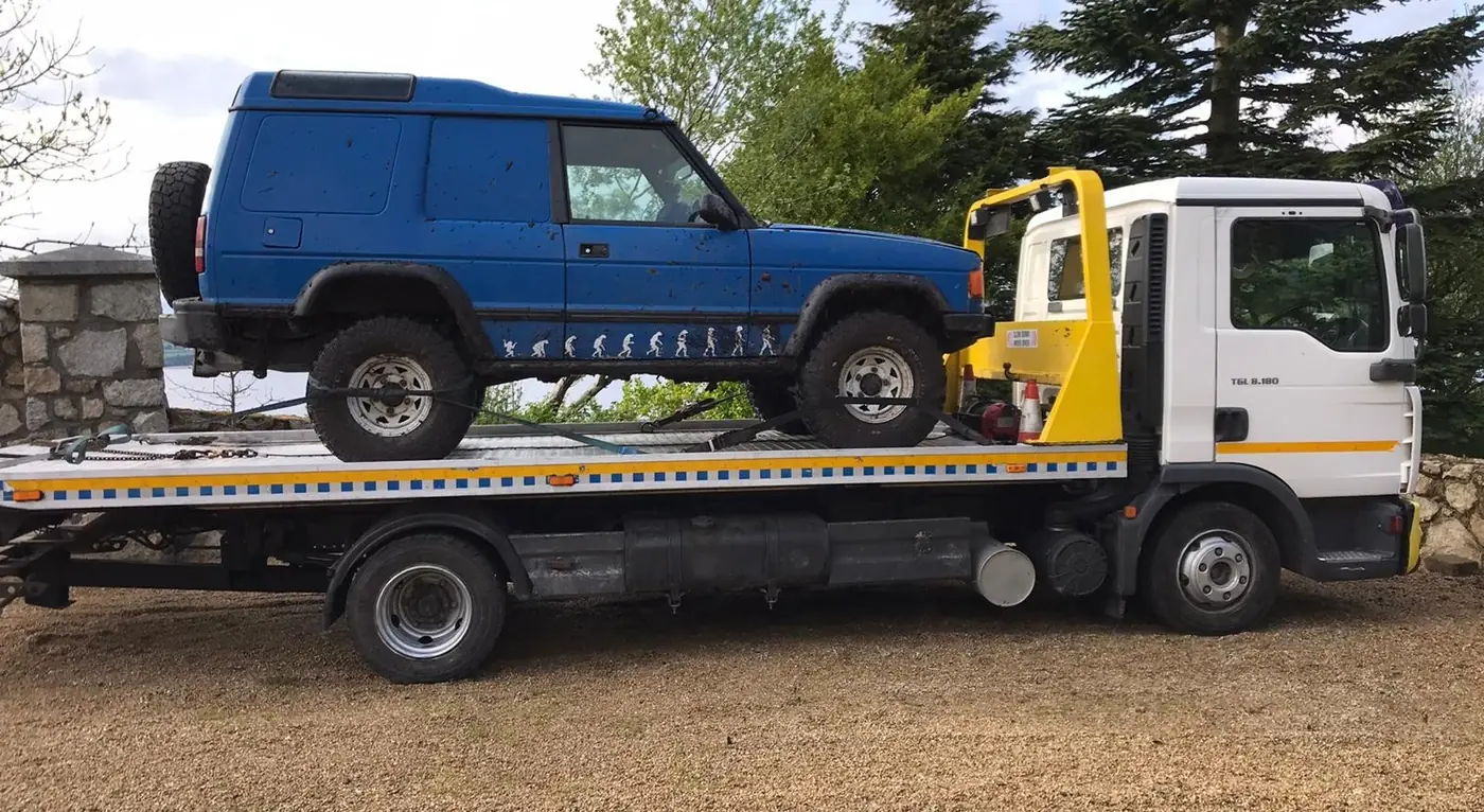 An older 4x4 loaded on a flatbed recovery truck
