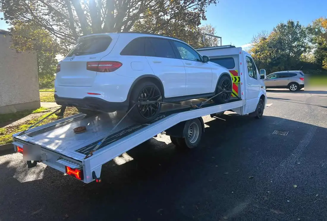 A white SUV on the tilted bed of a CC Recovery flatbed, being strapped down
