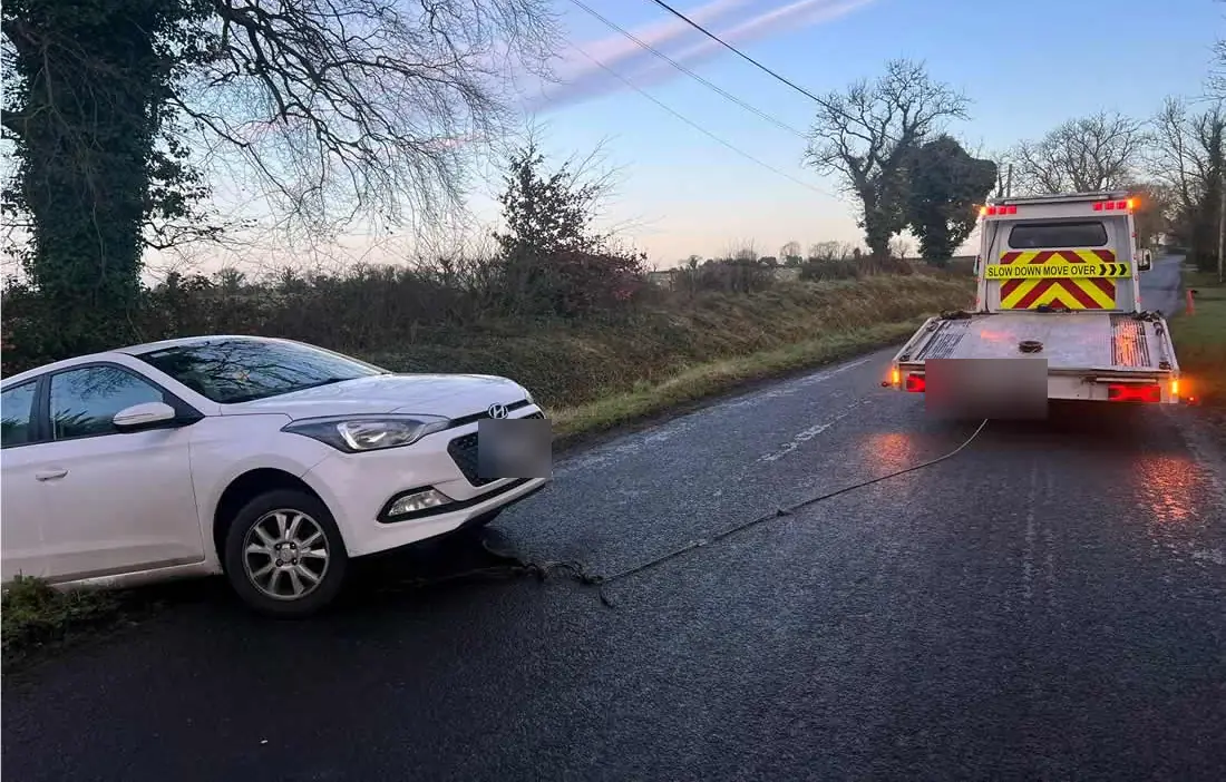 A white hatchback on a grass verge on a Meath country road, a CC Recovery truck behind it with a line attached