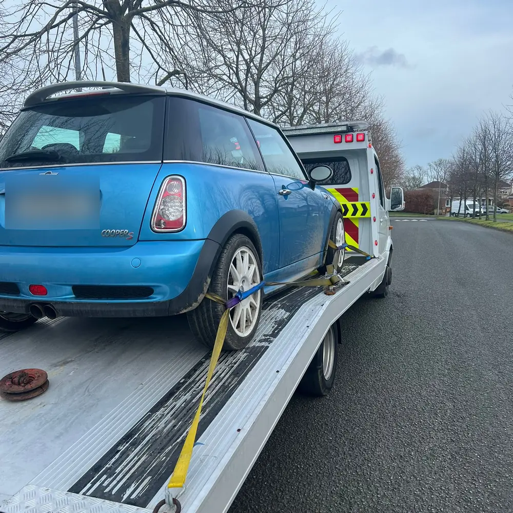 A blue Mini Cooper strapped onto the flatbed of a CC Recovery truck