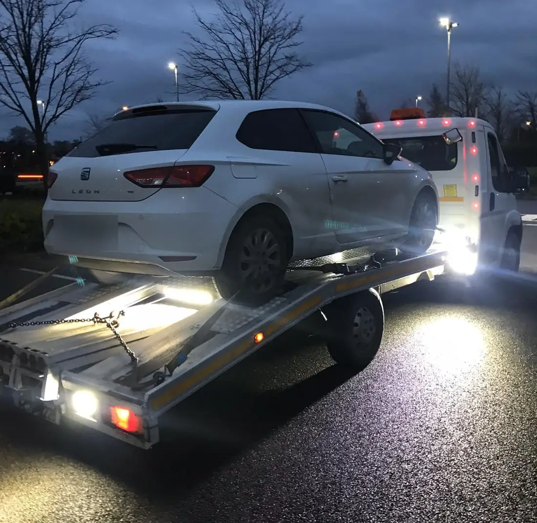 Night-time towing: a white hatchback loaded under the work lights