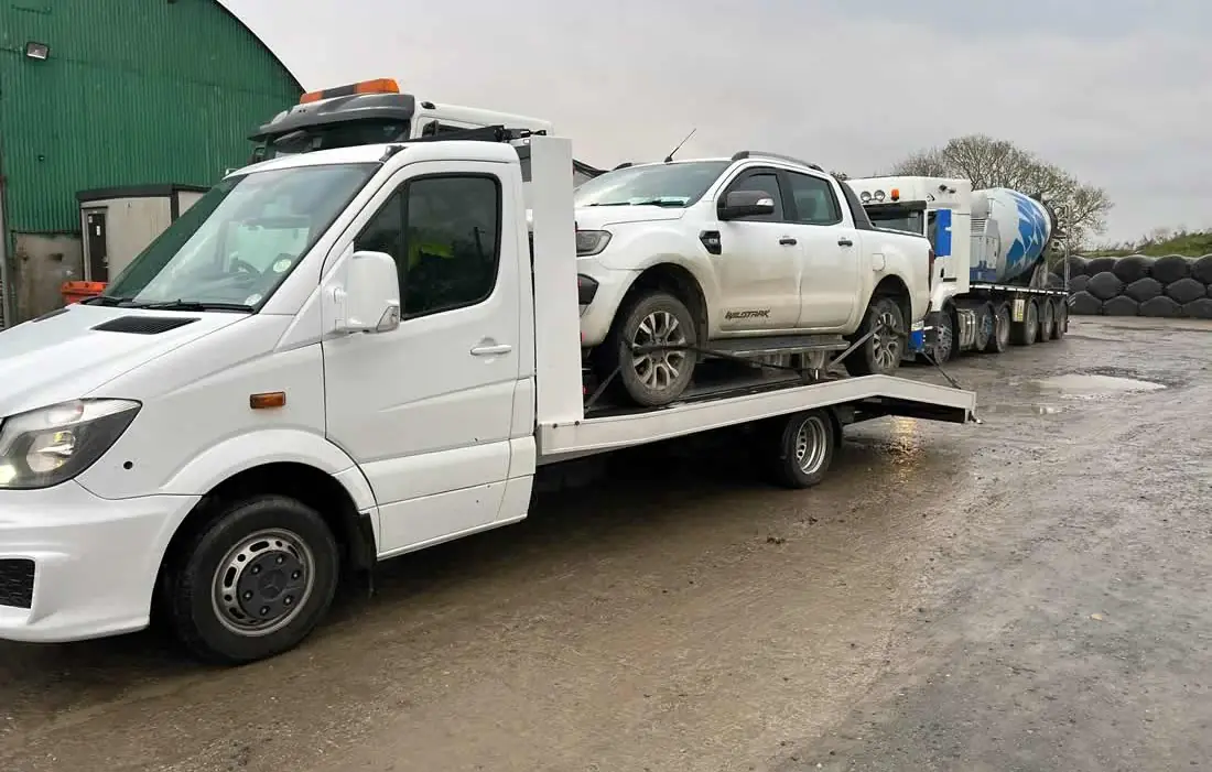 A white pick-up on the deck of a CC Recovery truck in a farmyard