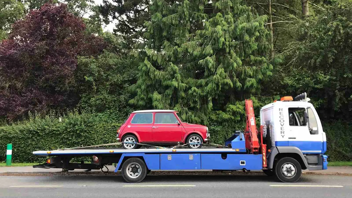 A classic red Mini on a crane-equipped recovery truck
