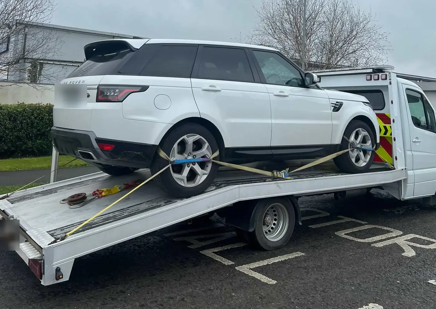 A white SUV being strapped down on the tilted bed of a CC Recovery flatbed
