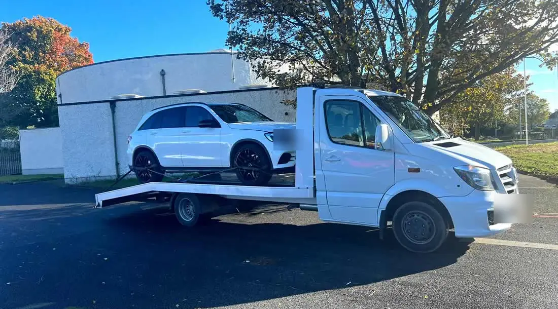 A white CC Recovery Sprinter flatbed carrying a white SUV on a bright day