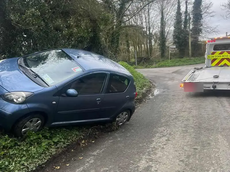 A small car up on a steep verge at a country junction